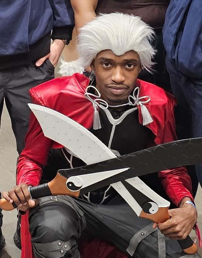 Hugues cosplaying at a comic-con, wearing a white wig and holding two curved blades.
