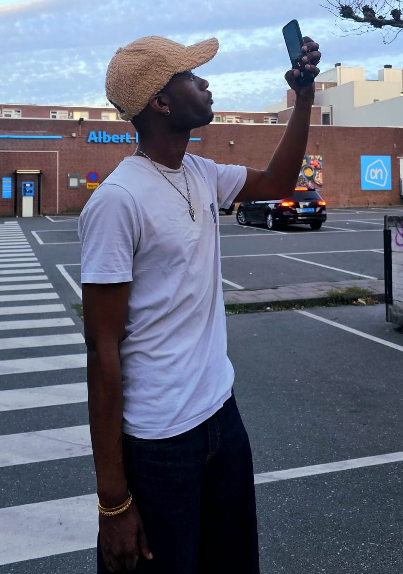 Hugues Nzeyimana standing outside, taking a photo on his phone.